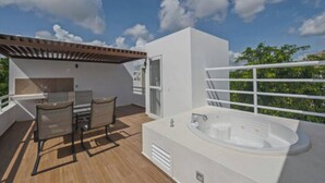Una terraza en la azotea con un jacuzzi, una mesa con sillas y una pérgola.
