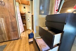 Een kleine kamer met een stapelbed, houten vloer en een kast met daarop een 'WELCOME'-bord.