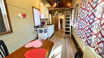 A room with a wooden dining table, a white cabinet, and a ladder leading to a loft area.