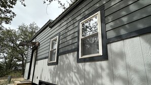Un petit bâtiment en bois d’un seul étage, doté de deux fenêtres et d’une porte, d’un petit porche avec des marches et d’une remorque attelée.