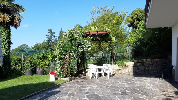 A stone patio with white chairs and a table, surrounded by greenery and a stone wall. - red fountain house (arizzano)