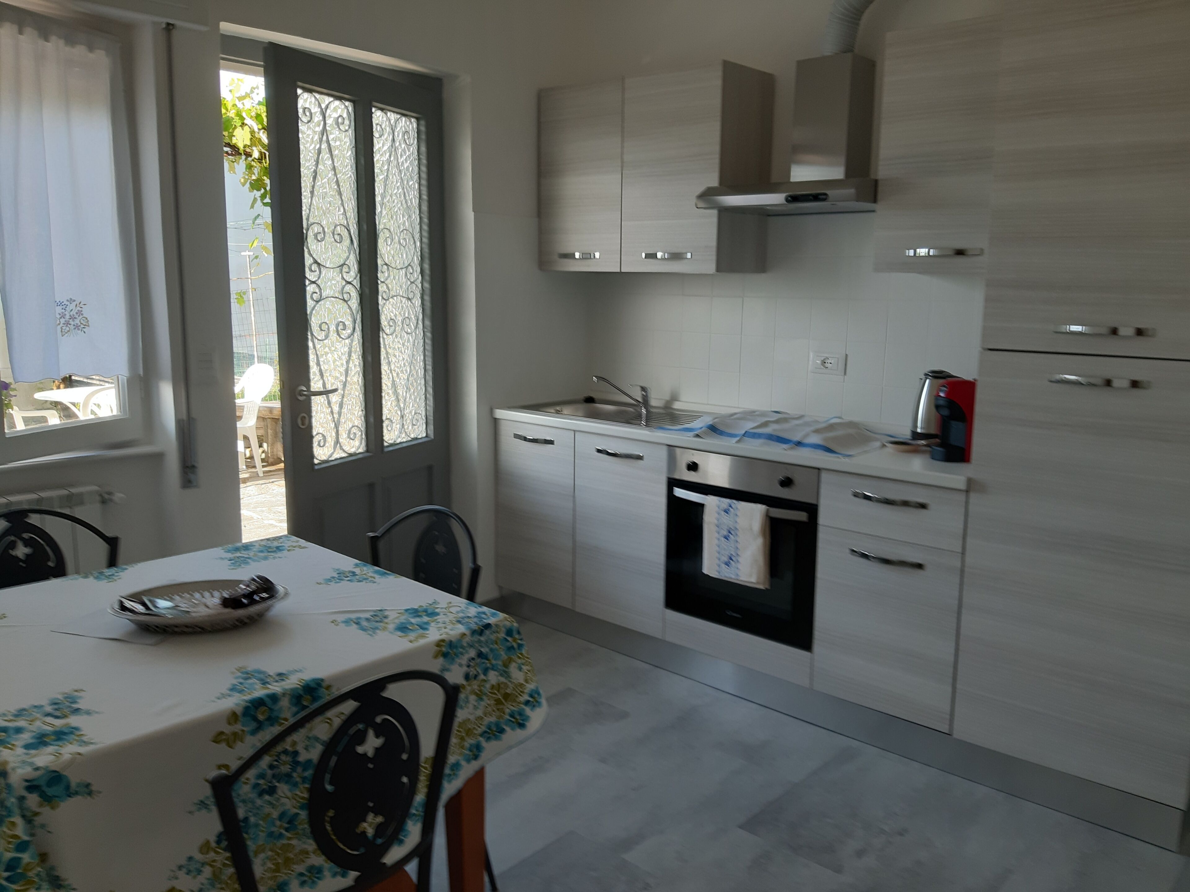 Uma cozinha moderna com área de refeições, apresentando uma mesa com toalha de mesa florida, forno embutido e pia de aço inoxidável.