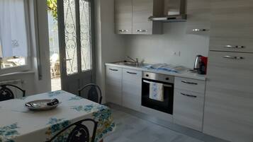 Uma cozinha moderna com área de refeições, apresentando uma mesa com toalha de mesa florida, forno embutido e pia de aço inoxidável.