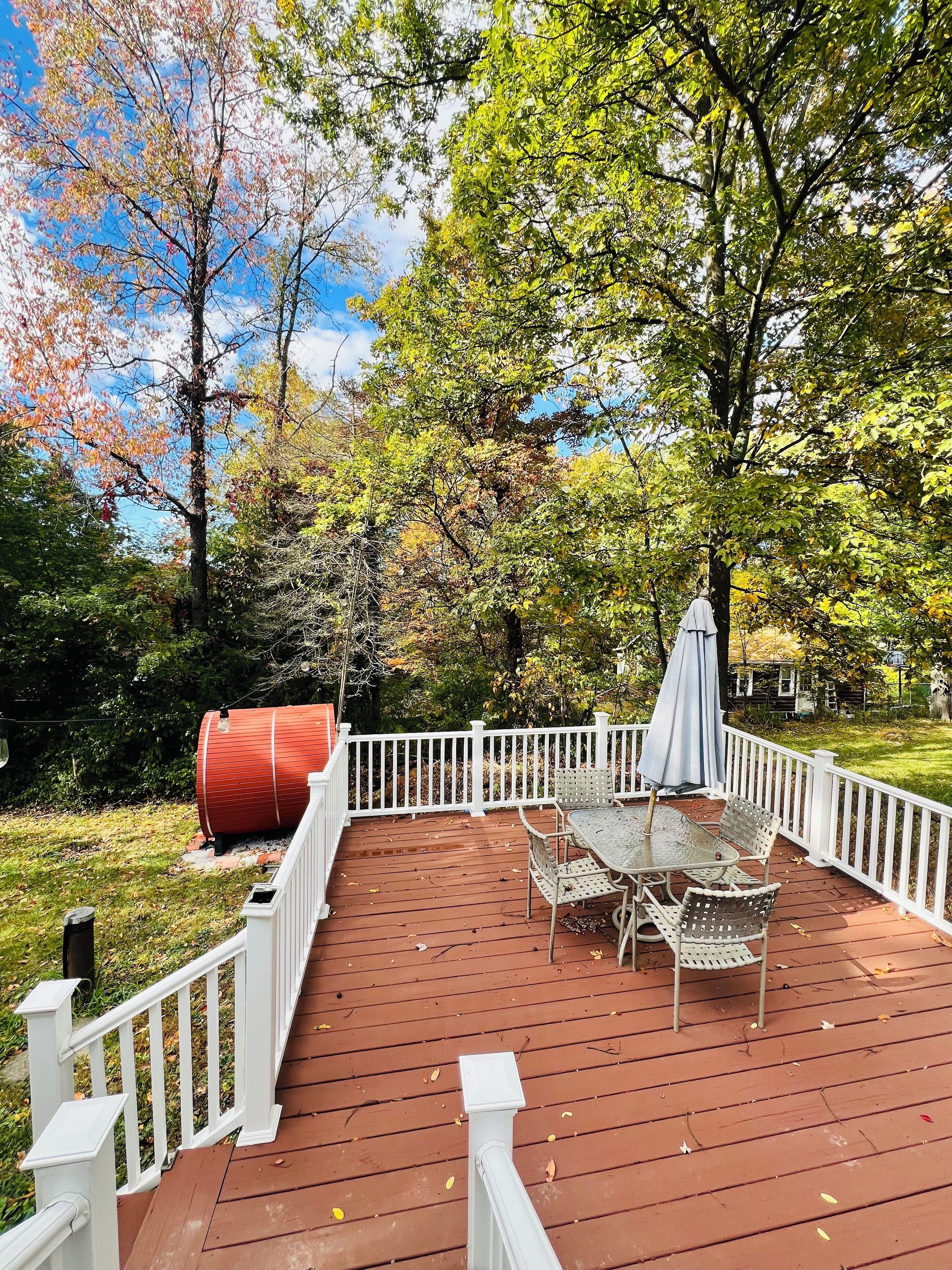 A wooden deck with a white railing, a table with chairs, and a red barrel.