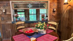 A wooden interior with a round table, chairs, a bowl of red apples, a vase of flowers, and a sign reading "up it simple". - Cozy Cabin with Sauna & Firepit! (Monroe)