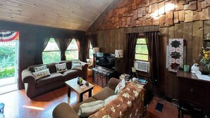 A cozy living room with a wooden ceiling and walls, a sofa set, a coffee table, a TV, and a decorative mirror. - Cozy Cabin with Sauna & Firepit! (Monroe)