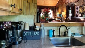 A cozy kitchen with wooden walls, a coffee bar, and a large window with stained glass. - Cozy Cabin with Sauna & Firepit! (Monroe)