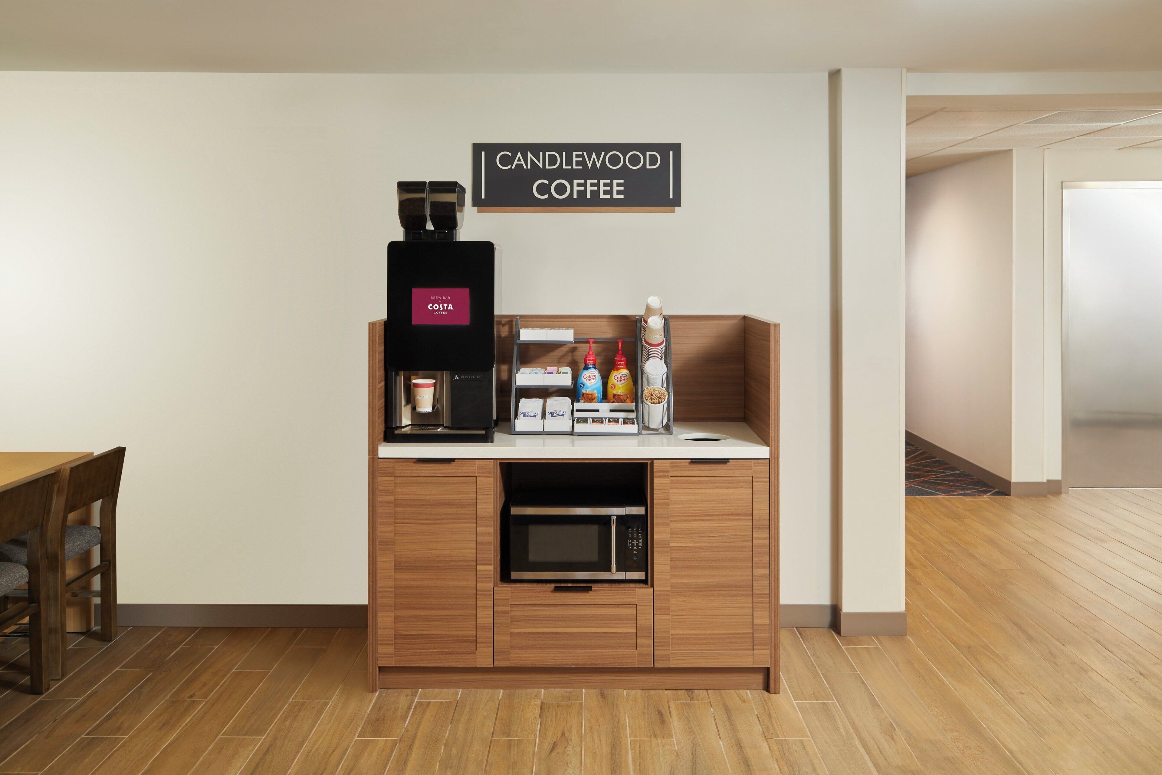 A coffee station with a coffee machine, milk and sugar dispensers, and a sign reading 'CANDLEWOOD COFFEE'.