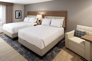 Una habitación de hotel con dos camas, un sofá, una mesita de noche con lámpara y una ventana con cortinas.