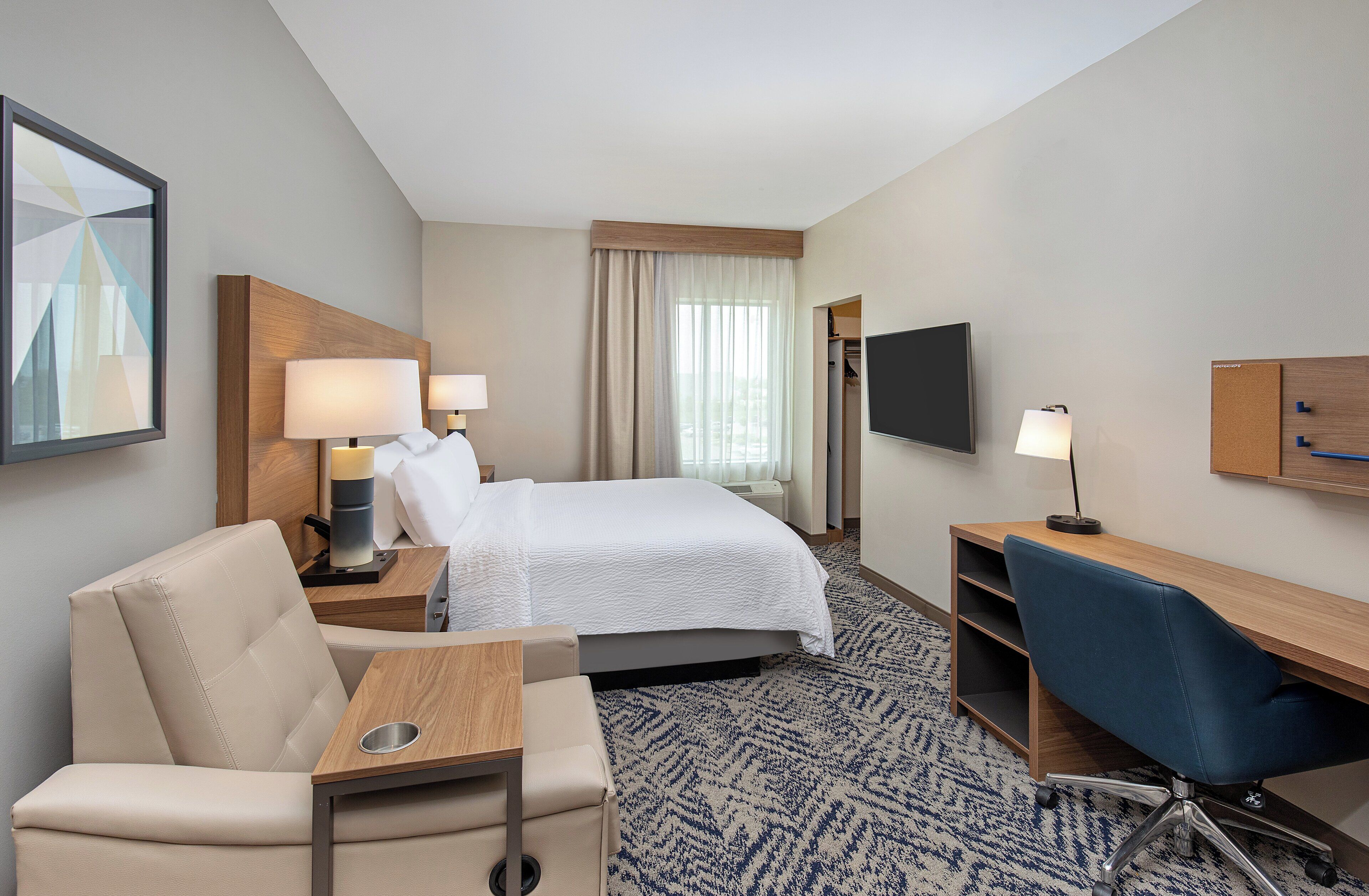 A hotel room with a bed, a desk, a chair, a TV, and a window with curtains.
