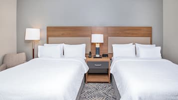 A hotel room with two beds, a nightstand with a lamp, and a small drawer.