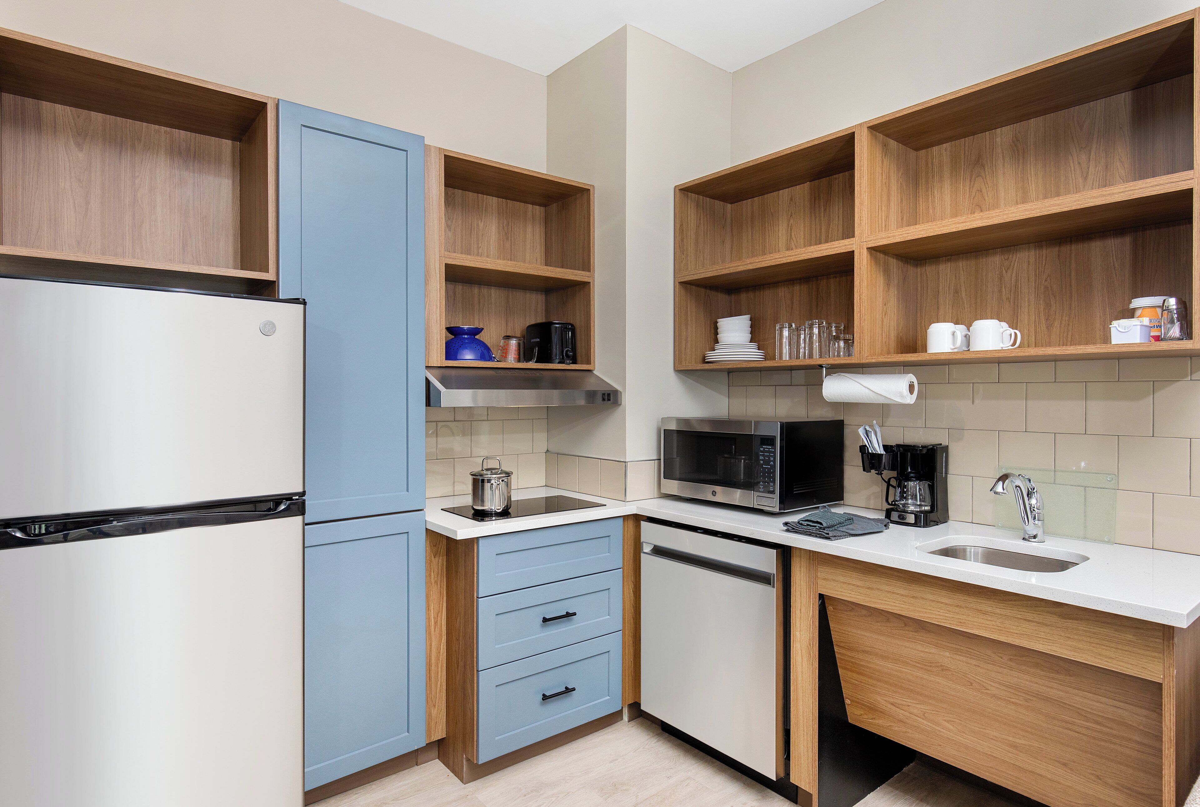 Una cucina compatta con frigorifero, microonde, lavandino ed scaffali in legno.