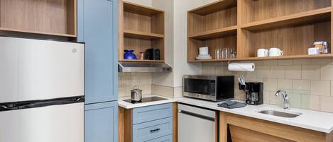 Una cucina compatta con frigorifero, microonde, lavandino ed scaffali in legno.