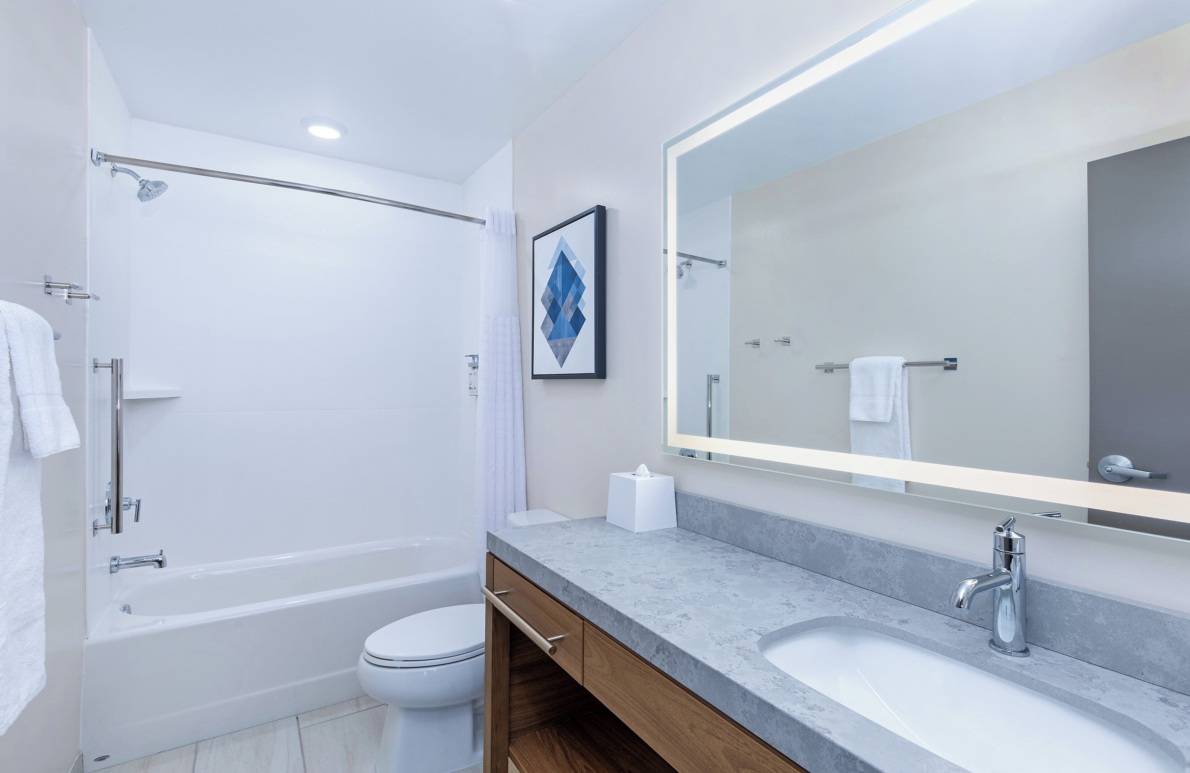 A modern bathroom with a bathtub, toilet, and a large mirror above the sink.