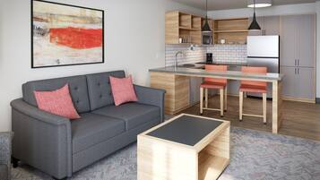 A modern living room with a grey sofa, a coffee table, and a kitchen area with wooden cabinets and a central island.