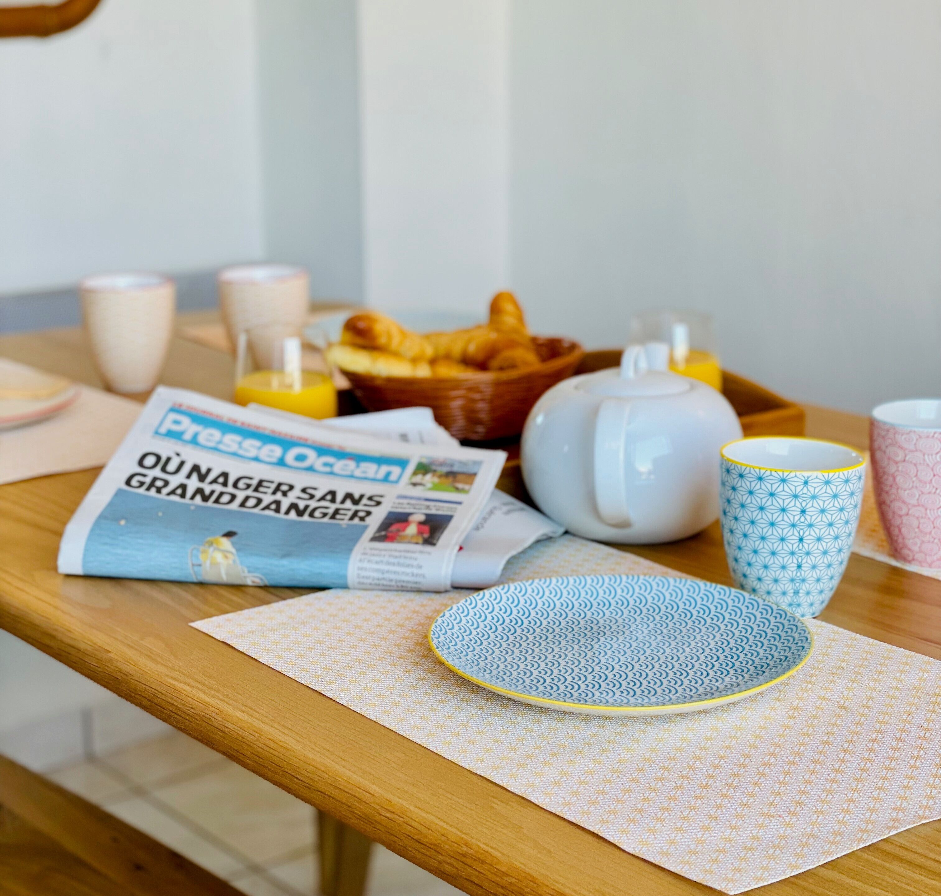 Una mesa de desayuno con un periódico, croissants, un hervidor de té y tazas.