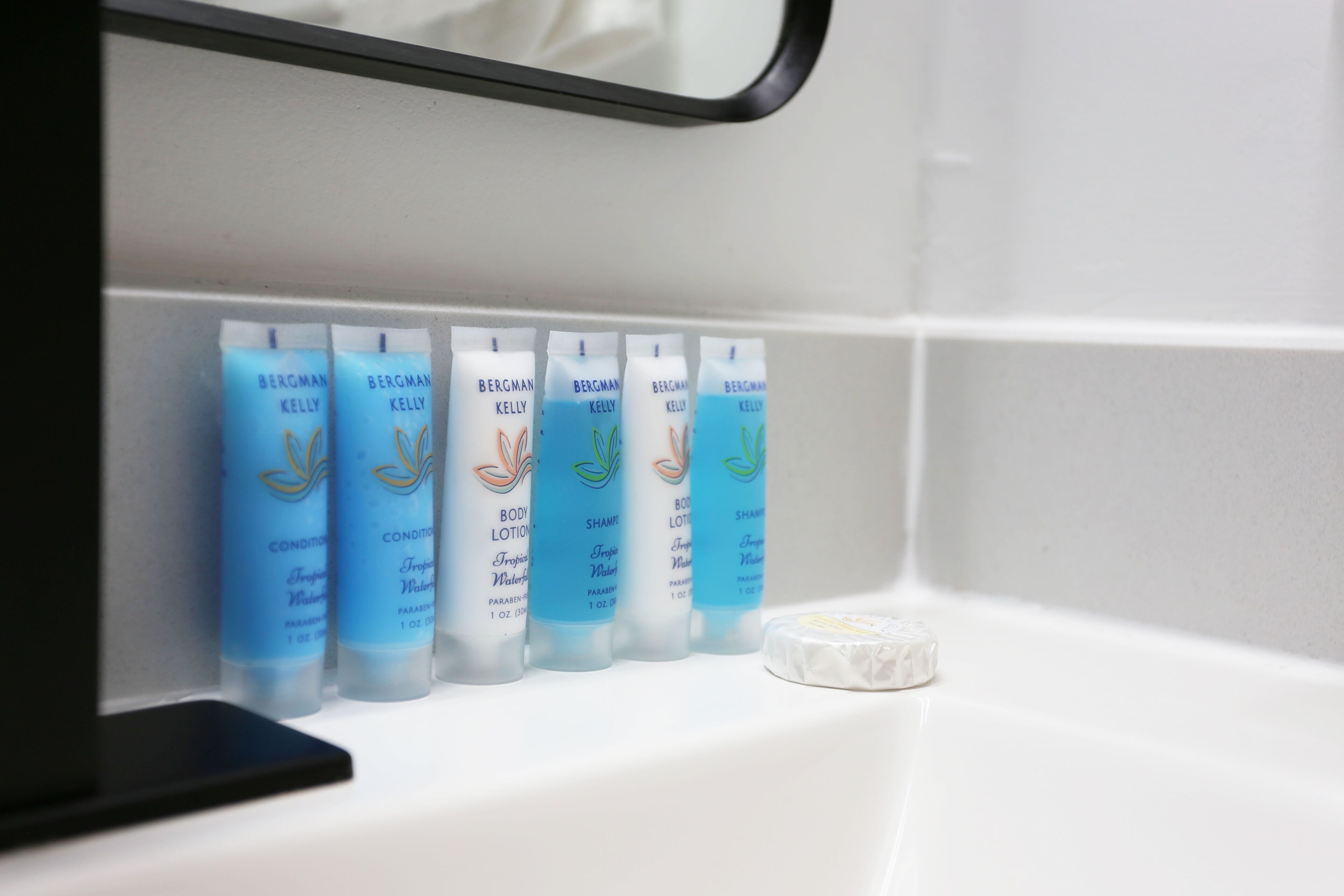 A bathroom shelf with five bottles of Bergman Kelly body lotion and a bar of soap.