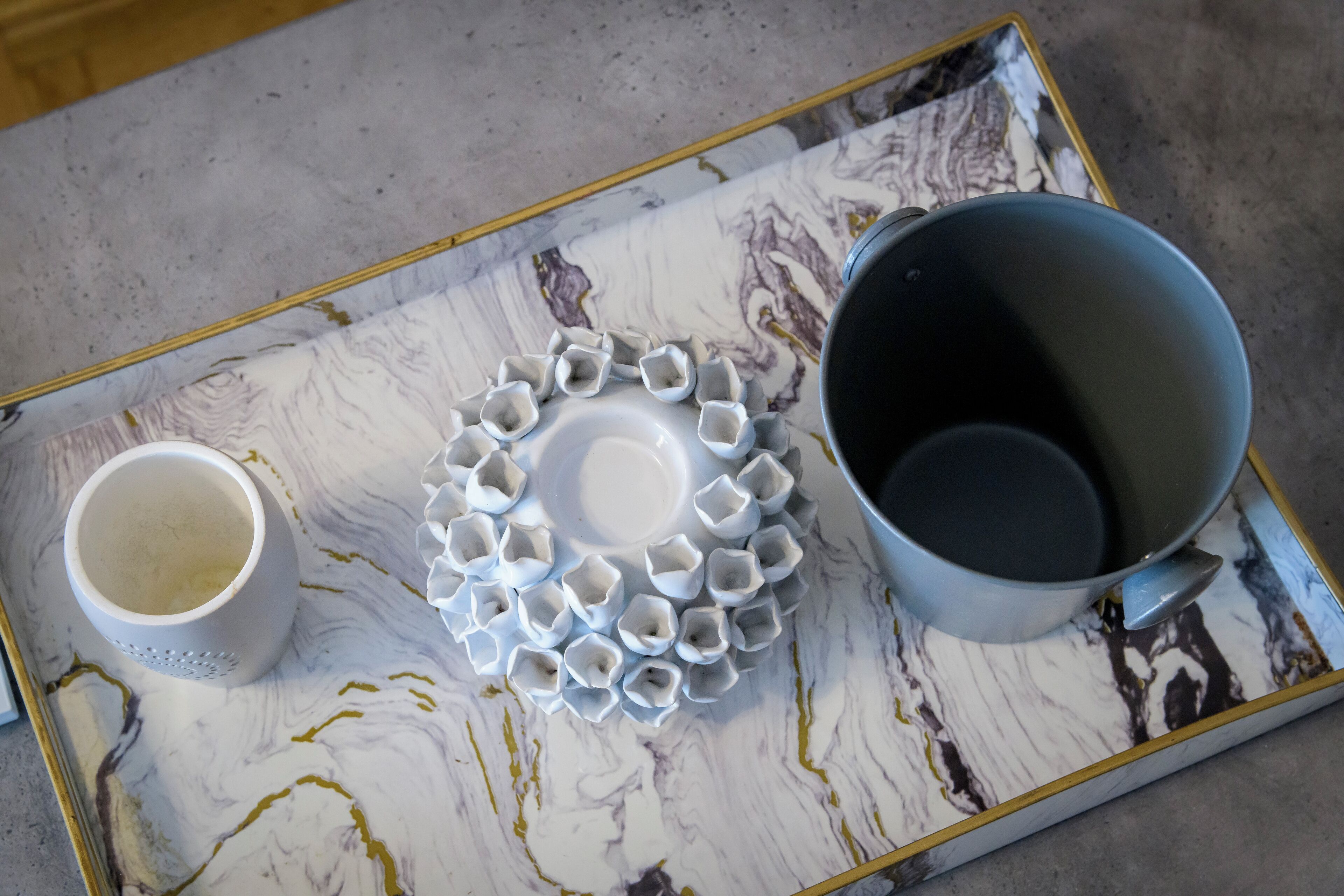 A tray with a white and gold marble pattern, a white mug, and a gray pot.