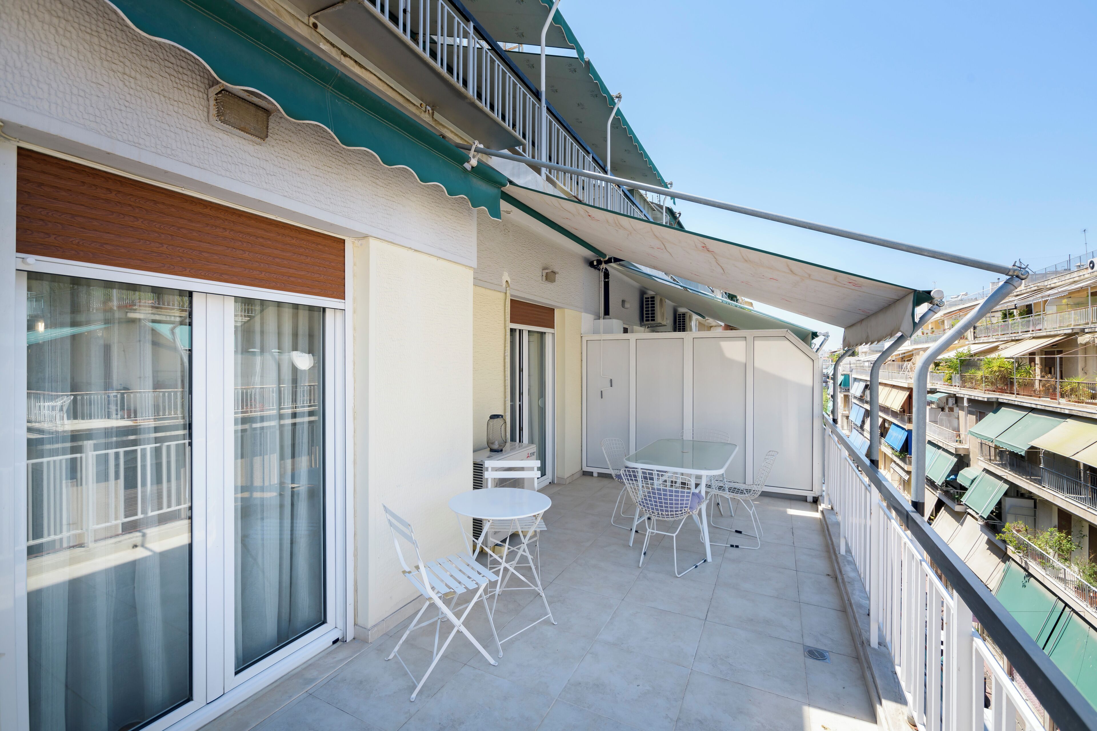 Ein Balkon mit Tisch und Stühlen, eine Schiebeglastür und Blick auf benachbarte Gebäude.