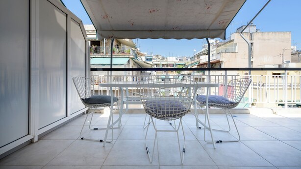 Ein Balkon mit einem weißen Metalltisch und -stühlen, ein weißes Markisenverdeck und Blick auf Gebäude im Hintergrund.