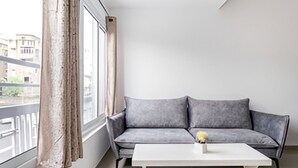 Een moderne woonkamer met een grijze bank, een witte salontafel en een uitzicht op gebouwen door een raam met gordijnen.