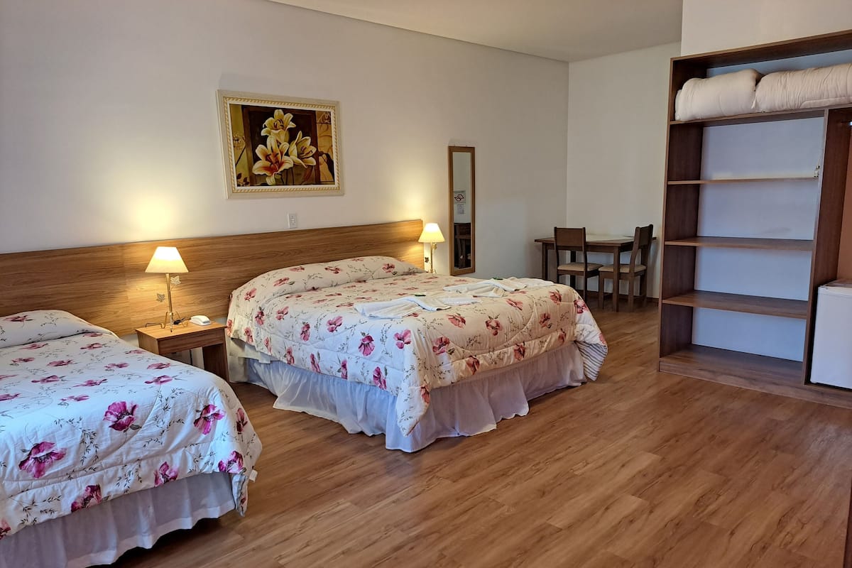 A hotel room with two beds, wooden headboards, a wooden wardrobe, a desk, and a chair.