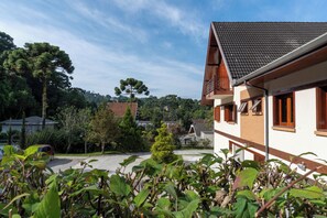 A residential building with a sloped roof, a balcony, and a driveway leading to a parked car. - Pousada Recanto Feliz (Campos do Jordão)