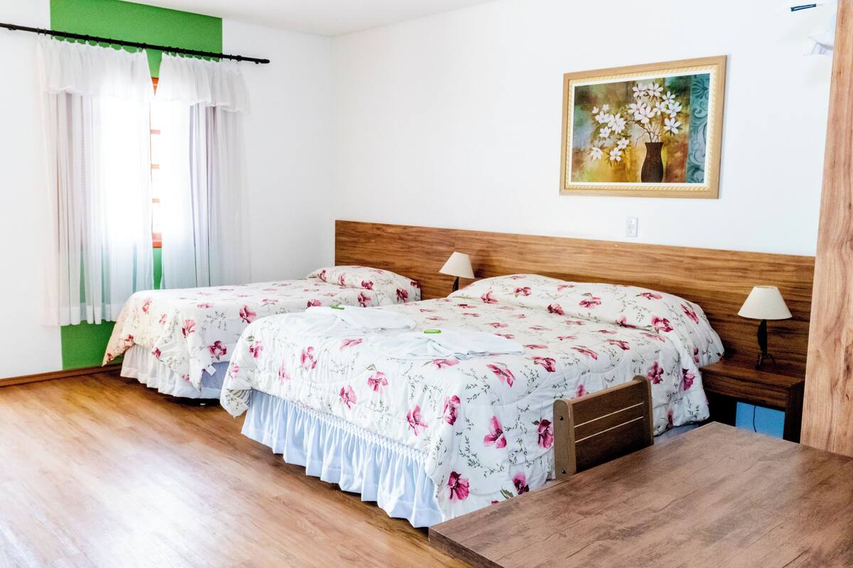 A double bed with floral bedding, a wooden headboard, a bedside table with a lamp, and a painting on the wall.