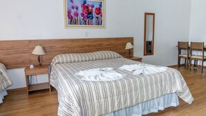 Una habitació d'hotel amb un llit gran, dues taules de nit amb làmpades, un mirall i un quadre de flors a la paret.