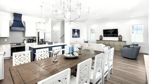 A modern kitchen with white cabinetry, a wooden dining table, and a chandelier. - Vista! Ocean Views from rooftop deck! (Destin)