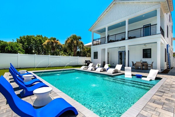 A modern two-story house with a swimming pool, lounge chairs, and a covered patio area.