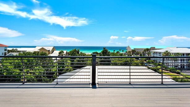A coastal view with a clear sky, a metal railing, and buildings in the background. - Vista! Ocean Views from rooftop deck! (Destin)