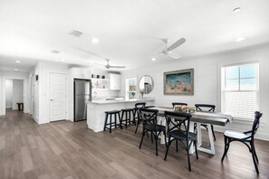 A modern kitchen with white cabinetry, a stainless steel refrigerator, and a dining area with a table and chairs.