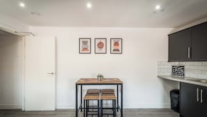 A kitchen with a white door, a table with two chairs, and three framed pictures on the wall. - Two Bedroom Apartment, Sleep 5, Old Swan (Old Swan)