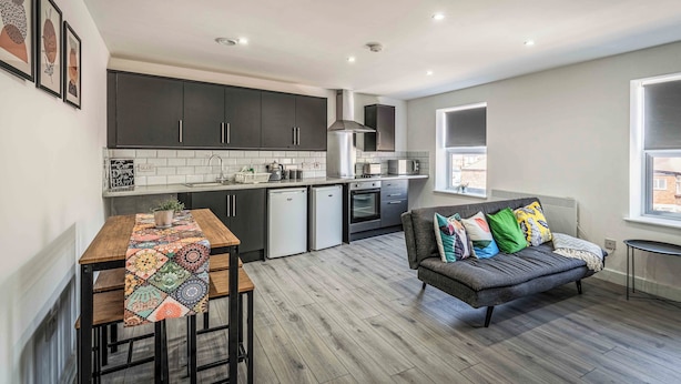 A modern kitchen with dark cabinets, a dining table with a colorful table runner, and a gray sofa with colorful pillows. - Two Bedroom Apartment, Sleep 5, Old Swan (Old Swan)