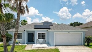 Une maison de plain-pied avec un garage, une porte d’entrée et un petit patio aménagé avec des chaises.