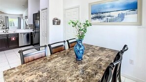Un coin repas avec une table en marbre, des chaises, un vase de fleurs, un lustre et un tableau au mur.