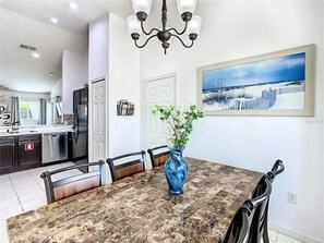 A dining area with a marble table, chairs, a vase with flowers, a chandelier, and a painting on the wall. - Hillcrest Hideaway, Peaceful 4 Bed Pool Home with Games and Minutes from Disney (Davenport)