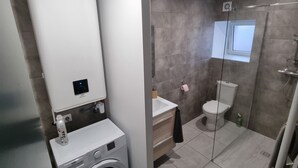 Un baño moderno con lavadora integrada, inodoro y zona de ducha.
