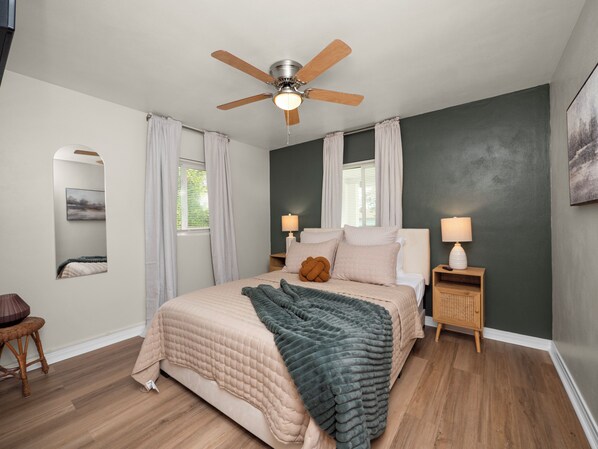 A bedroom with a bed, two bedside tables, a ceiling fan, and a window with curtains. - Charming Home Close to Downtown, Fully Renovated (Lakeland)
