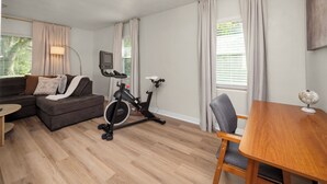 Ein Wohnzimmer mit einer Couch, einem Esstisch, einem Sessel, einem Heimtrainer und einer Lampe.
