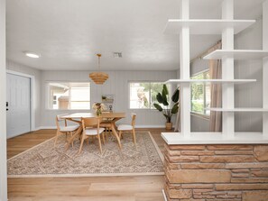 A dining area with a wooden table and chairs, a hanging light fixture, and a view of the outdoors through large windows. - Charming Home Close to Downtown, Fully Renovated (Lakeland)