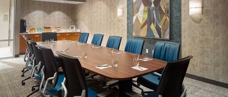 Un salón de conferencias con una mesa larga, sillas azules y un cuadro abstracto moderno en la pared.