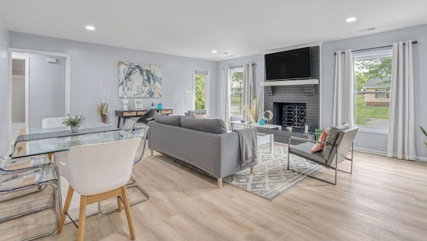 A modern living room with a glass dining table, grey sofa, and a fireplace. - Stylish Home Near Uptown, UNC, and More! (Charlotte)