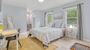 A bedroom with a bed, bedside table, lamp, and a view of the outdoors through a window. - Stylish Home Near Uptown, UNC, and More! (Charlotte)