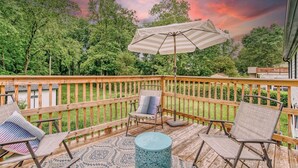 A wooden deck with outdoor furniture, including two chairs and a table, and a large umbrella. - Stylish Home Near Uptown, UNC, and More! (Charlotte)
