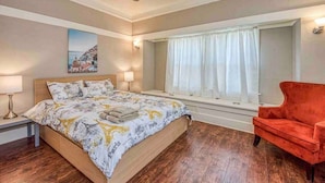 Un dormitorio con una cama, una ventana con cortinas, una silla roja y un ventilador de techo.