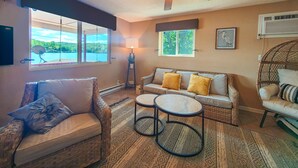 A cozy living room with a ceiling fan, a sofa with cushions, a small table, and a window overlooking a scenic view.