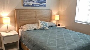 A bedroom with a bed, two bedside tables with lamps, a ceiling fan, a painting on the wall, and a window.