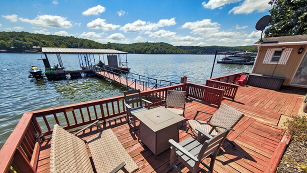 A wooden deck with outdoor furniture, a table, and a view of the lake and dock.